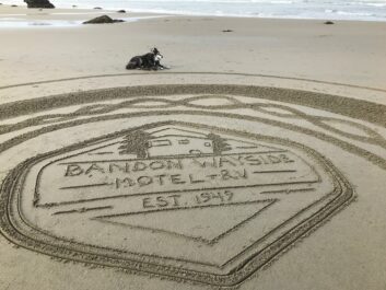 Drawing in sand of Bandon Wayside Motel + RV logo with dog lying on sand