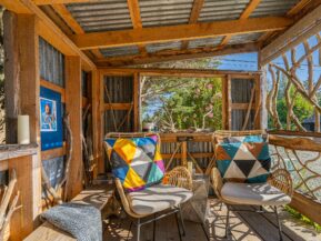 photo of a b.side motel and rv park outdoor seating area with rattan chairs that have white cushions and colorful orange and blue and white accent pillows